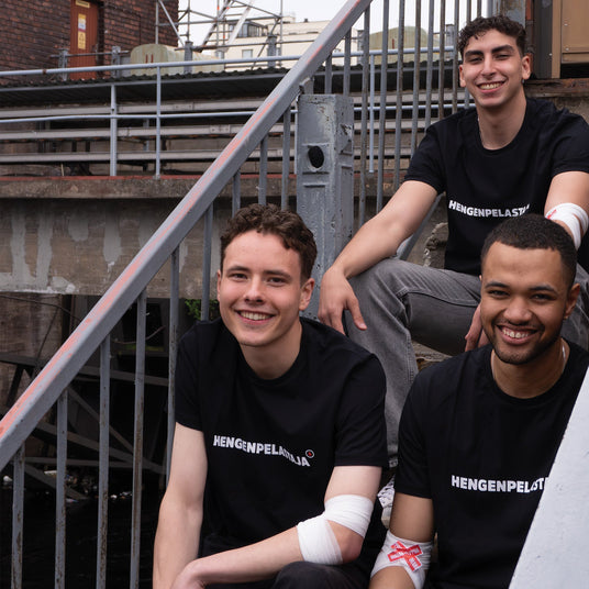 Kolme miestä istuu portailla mustat t-paidat päällä